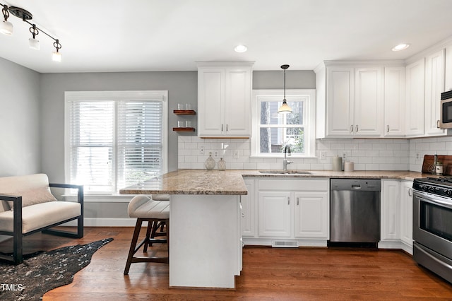 kitchen with white cabinets, appliances with stainless steel finishes, a kitchen breakfast bar, light stone countertops, and pendant lighting