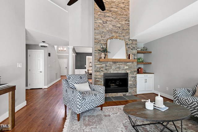 living area with decorative columns, baseboards, dark wood finished floors, a ceiling fan, and a fireplace