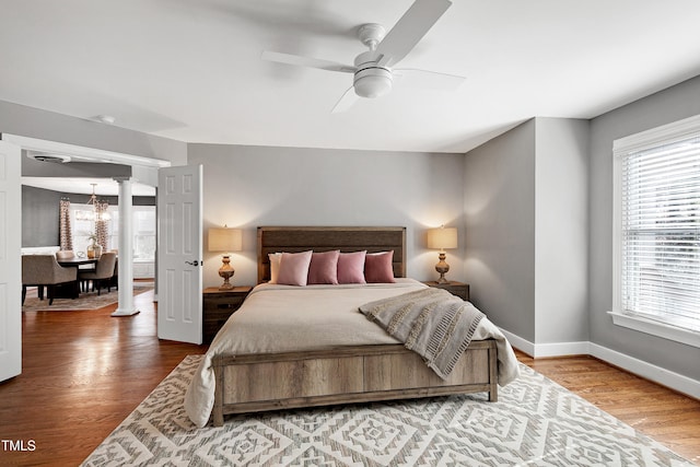 bedroom with ceiling fan with notable chandelier, wood finished floors, decorative columns, and baseboards