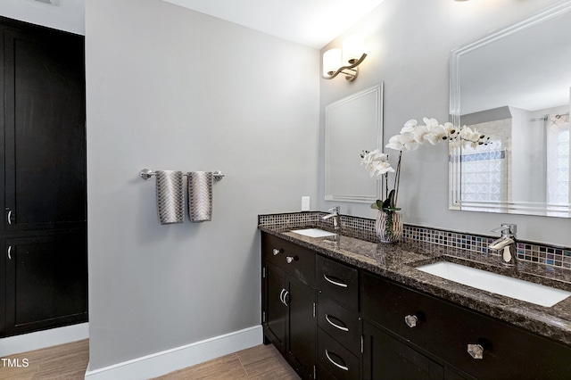 full bath featuring double vanity, wood finished floors, a sink, and baseboards