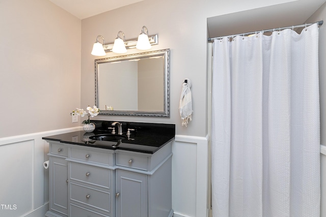 bathroom with curtained shower, vanity, a decorative wall, and wainscoting