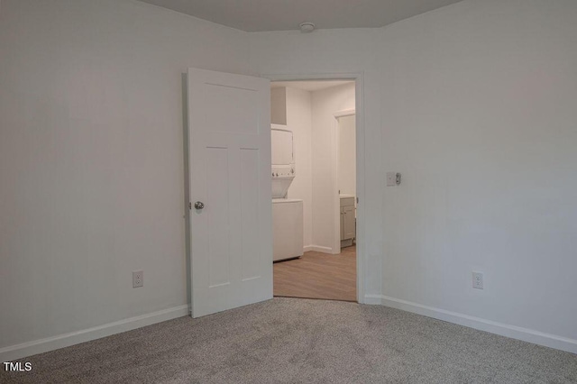 carpeted spare room featuring stacked washer / dryer