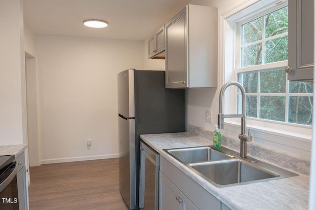 kitchen with gray cabinetry, light hardwood / wood-style flooring, stainless steel dishwasher, and sink