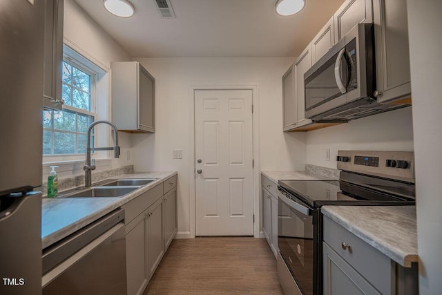 kitchen featuring gray cabinets, sink, stainless steel appliances, and light wood-type flooring