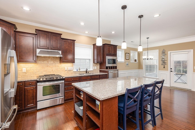 kitchen with stainless steel appliances, light stone counters, pendant lighting, a kitchen island, and ornamental molding