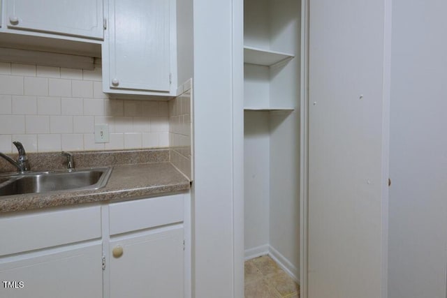 kitchen with tasteful backsplash, white cabinetry, sink, and light tile patterned floors