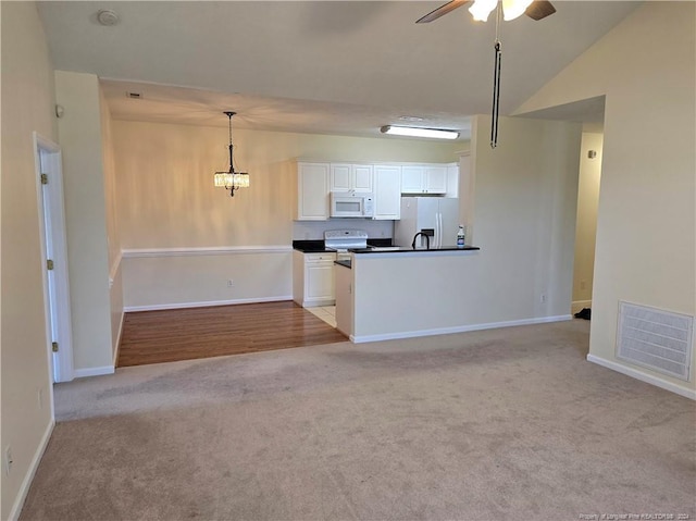 kitchen with white appliances, light colored carpet, vaulted ceiling, decorative light fixtures, and white cabinetry