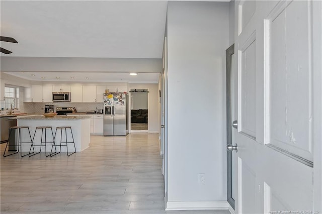 kitchen with tasteful backsplash, appliances with stainless steel finishes, a breakfast bar area, white cabinets, and light wood-type flooring