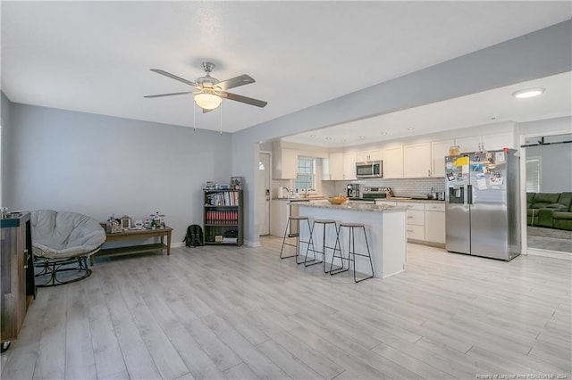 kitchen featuring a kitchen breakfast bar, white cabinetry, light wood-type flooring, and appliances with stainless steel finishes