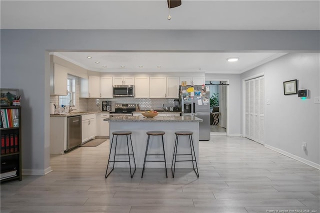 kitchen with a kitchen bar, white cabinets, appliances with stainless steel finishes, a kitchen island, and light stone counters