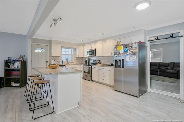 kitchen with kitchen peninsula, light stone counters, stainless steel appliances, light hardwood / wood-style floors, and white cabinetry