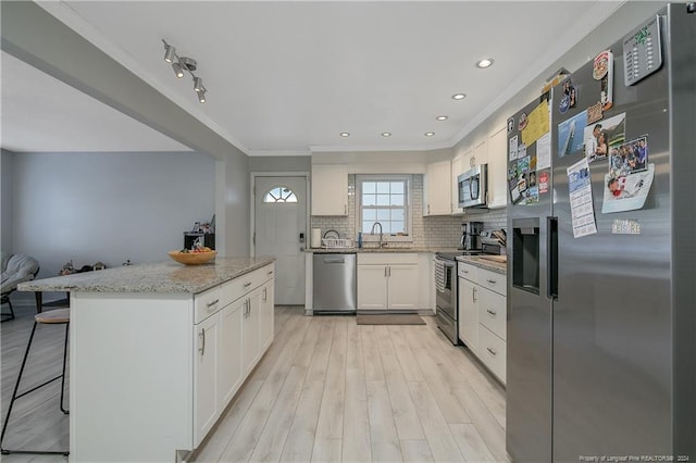 kitchen featuring a kitchen bar, appliances with stainless steel finishes, light wood-type flooring, light stone counters, and white cabinets