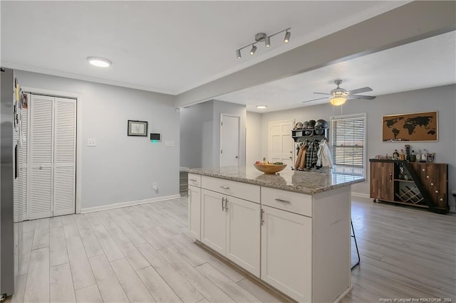 kitchen with light stone countertops, a center island, light hardwood / wood-style floors, and white cabinetry