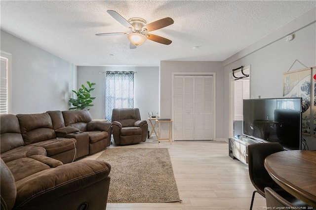 living room featuring ceiling fan, light hardwood / wood-style floors, and a textured ceiling