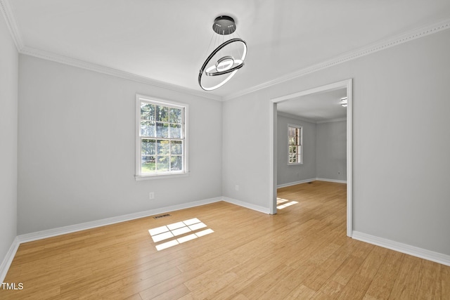 empty room with baseboards, visible vents, crown molding, and light wood finished floors