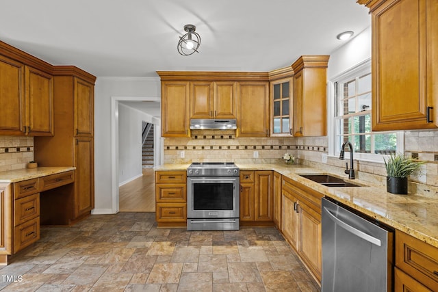 kitchen with brown cabinetry, appliances with stainless steel finishes, light stone countertops, under cabinet range hood, and a sink