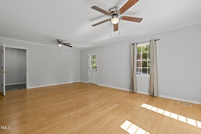 empty room featuring light wood-style floors, baseboards, visible vents, and crown molding