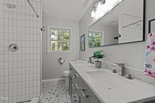 full bath with toilet, double vanity, a tile shower, and a sink