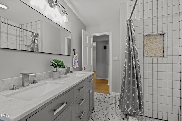 full bathroom with tiled shower, a sink, baseboards, and double vanity