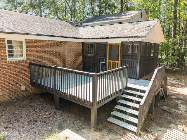 rear view of house with brick siding, a shingled roof, a wooden deck, and a sunroom