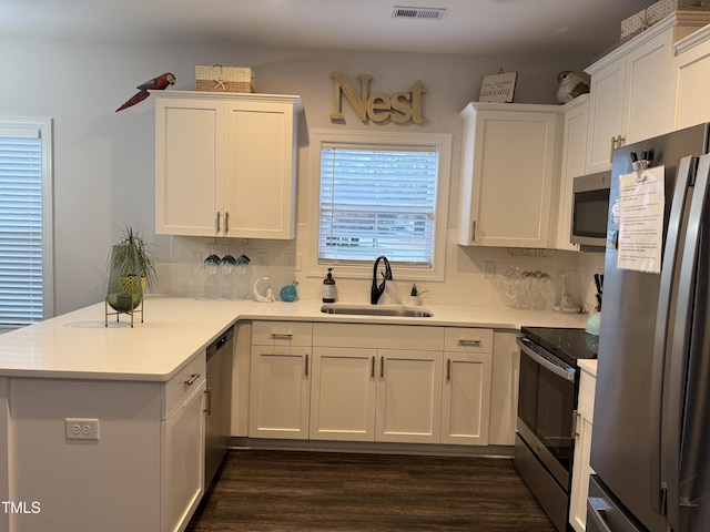 kitchen featuring kitchen peninsula, appliances with stainless steel finishes, decorative backsplash, sink, and white cabinetry