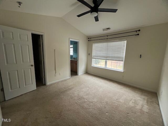 unfurnished bedroom featuring ceiling fan, a spacious closet, ensuite bathroom, vaulted ceiling, and light carpet