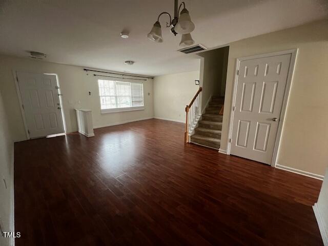 unfurnished living room with dark wood-type flooring and an inviting chandelier