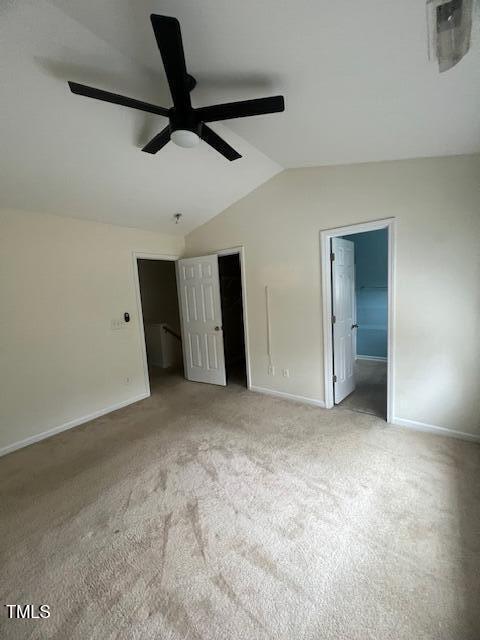 unfurnished bedroom with a walk in closet, vaulted ceiling, ensuite bath, ceiling fan, and light colored carpet