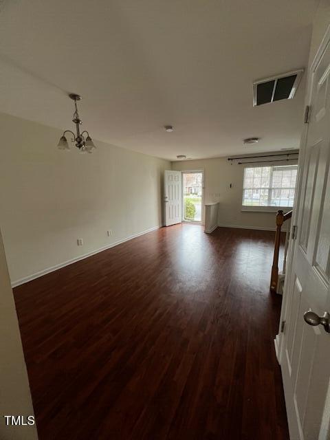 unfurnished room featuring dark wood-type flooring and an inviting chandelier