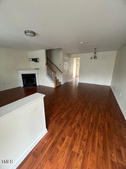 unfurnished living room featuring a notable chandelier and dark hardwood / wood-style floors