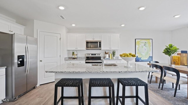 kitchen featuring stainless steel appliances, white cabinetry, a center island with sink, and light hardwood / wood-style flooring