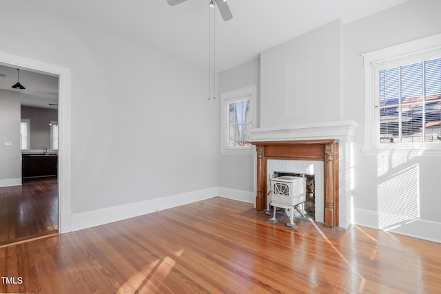 unfurnished living room with hardwood / wood-style flooring, a wood stove, sink, and ceiling fan