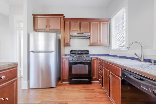 kitchen featuring light wood-type flooring, sink, light stone counters, and black appliances