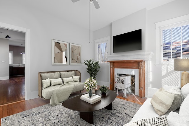 living room featuring sink, wood-type flooring, ceiling fan, and a wood stove