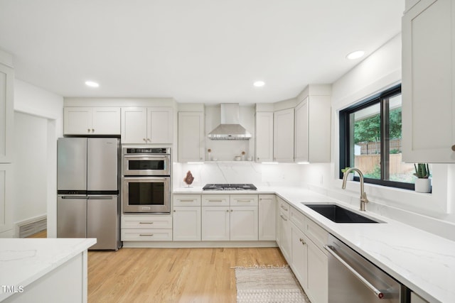 kitchen featuring stainless steel appliances, light stone countertops, wall chimney exhaust hood, white cabinets, and sink