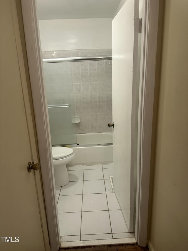 bathroom featuring tile patterned flooring, combined bath / shower with glass door, and toilet