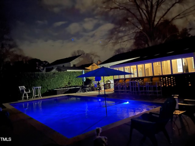 pool at night with grilling area and a wooden deck