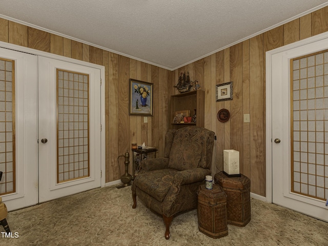 sitting room with carpet flooring, ornamental molding, a textured ceiling, and wooden walls