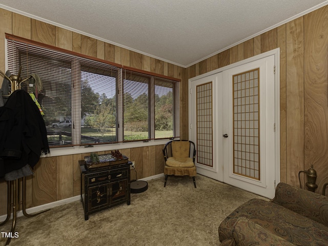 living area with light carpet, french doors, a textured ceiling, crown molding, and wooden walls