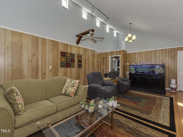 living room featuring a towering ceiling, ceiling fan with notable chandelier, a textured ceiling, hardwood / wood-style floors, and wood walls