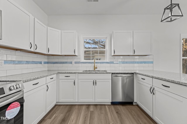 kitchen featuring appliances with stainless steel finishes, sink, wood-type flooring, white cabinetry, and hanging light fixtures