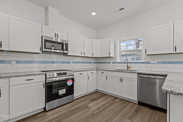 kitchen featuring tasteful backsplash, stainless steel appliances, sink, hardwood / wood-style floors, and white cabinetry