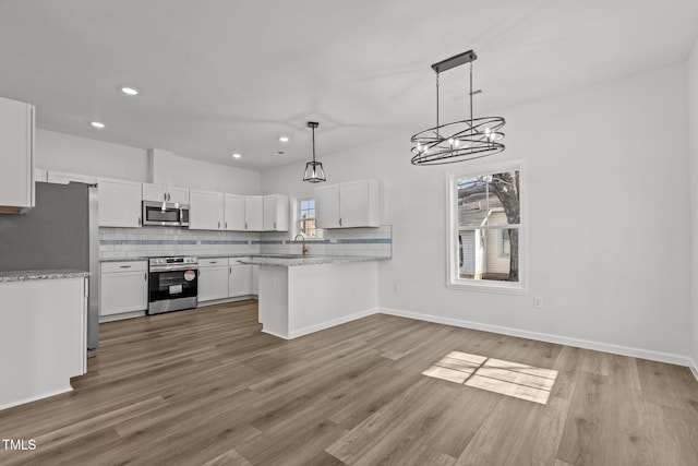 kitchen featuring kitchen peninsula, light wood-type flooring, stainless steel appliances, white cabinets, and hanging light fixtures