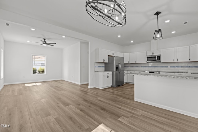 kitchen with light stone countertops, white cabinetry, stainless steel appliances, light hardwood / wood-style flooring, and ceiling fan with notable chandelier