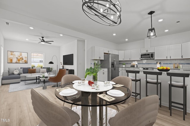 dining room with light hardwood / wood-style flooring and ceiling fan with notable chandelier