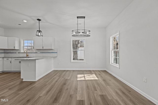 kitchen with decorative backsplash, light stone countertops, pendant lighting, light hardwood / wood-style flooring, and white cabinets