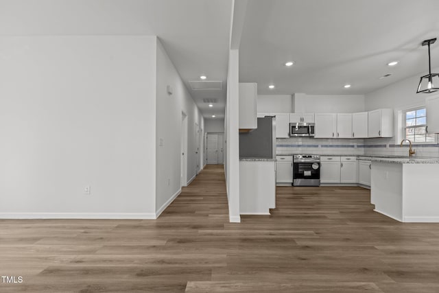 kitchen with light stone countertops, hanging light fixtures, appliances with stainless steel finishes, white cabinets, and hardwood / wood-style flooring