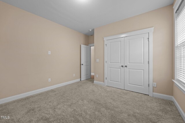 unfurnished bedroom with light colored carpet and a closet