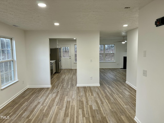 unfurnished living room featuring ceiling fan, a fireplace, light hardwood / wood-style floors, and a textured ceiling