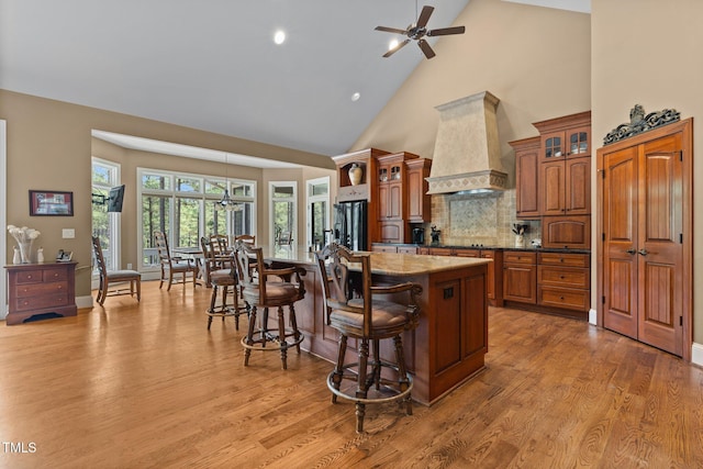 kitchen with hardwood / wood-style floors, premium range hood, high vaulted ceiling, a kitchen island with sink, and a breakfast bar area